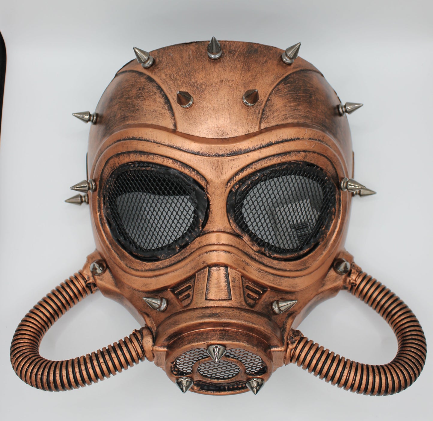 A steampunk-style copper-colored gas mask with black mesh eye panels, metal spikes, and corrugated breathing tubes.